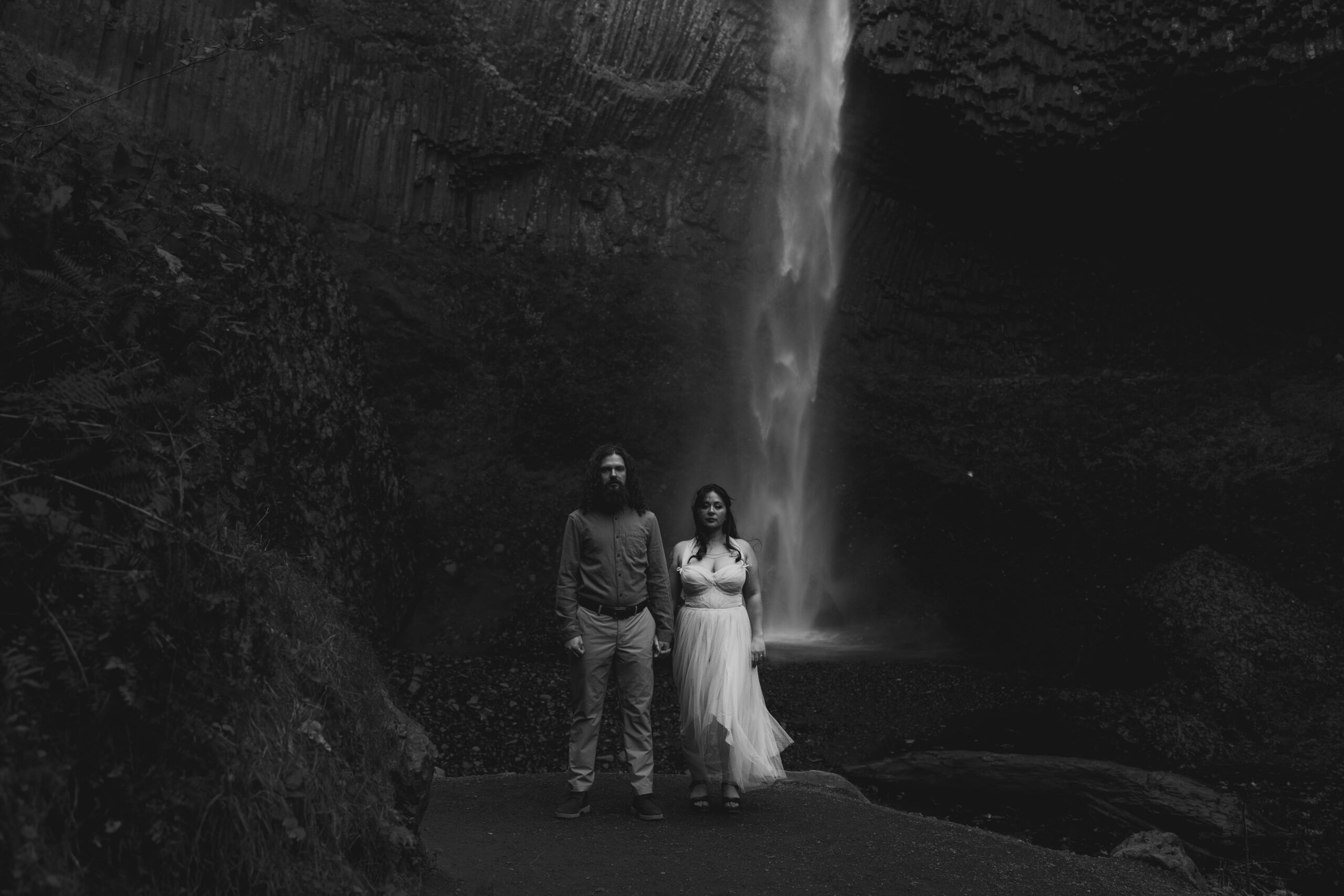 couple standing on pathway with waterfall in distance behind them in black and white