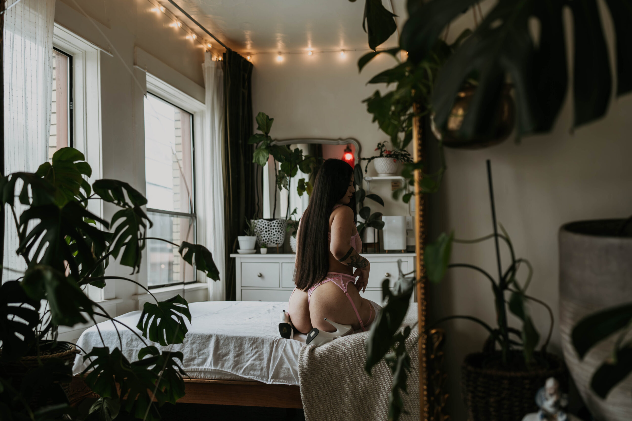 women sitting on bed for boudoir while back is towards mirror and photographer is shooting through mirror