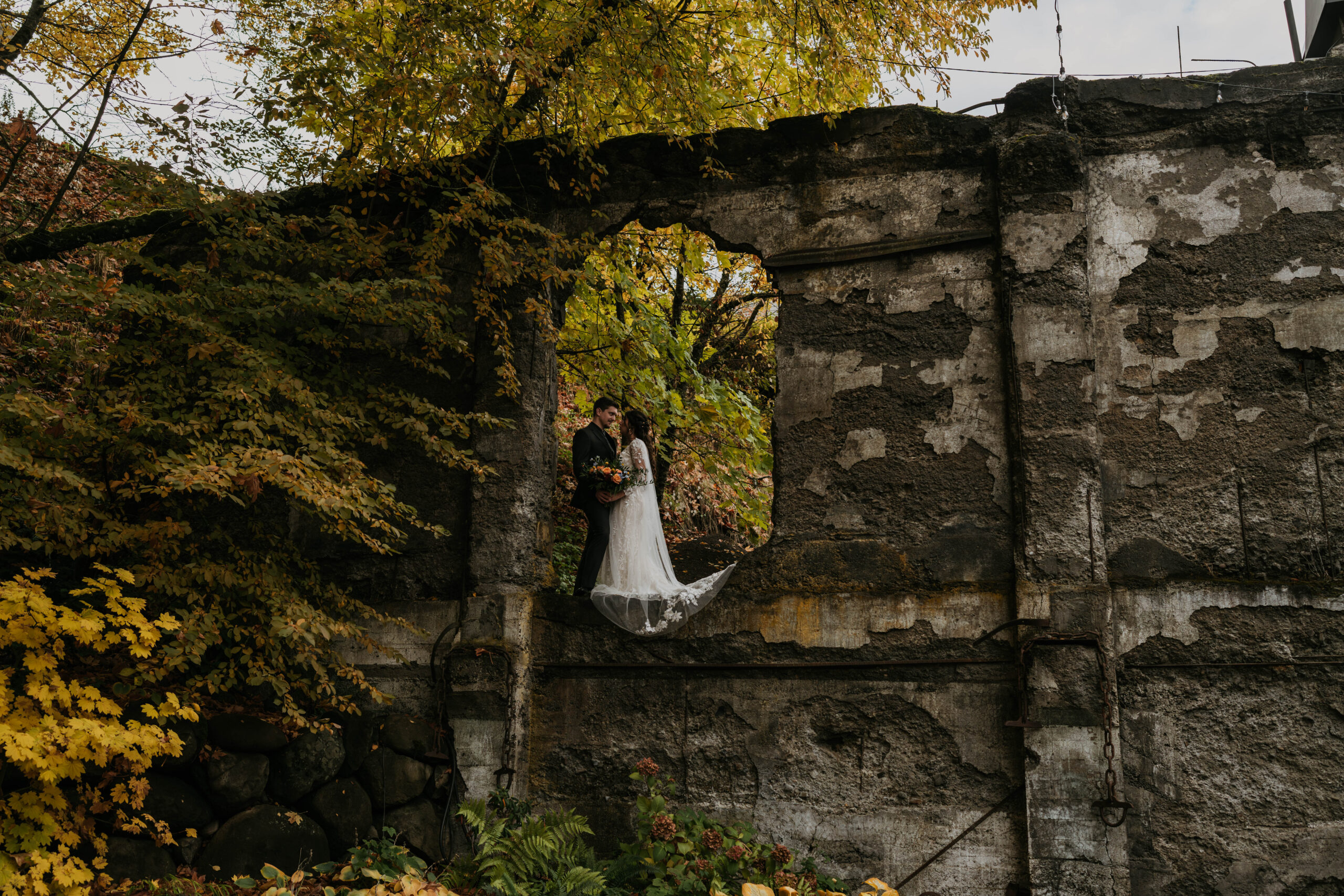 Bride and groom kissing under stone arch in forest
