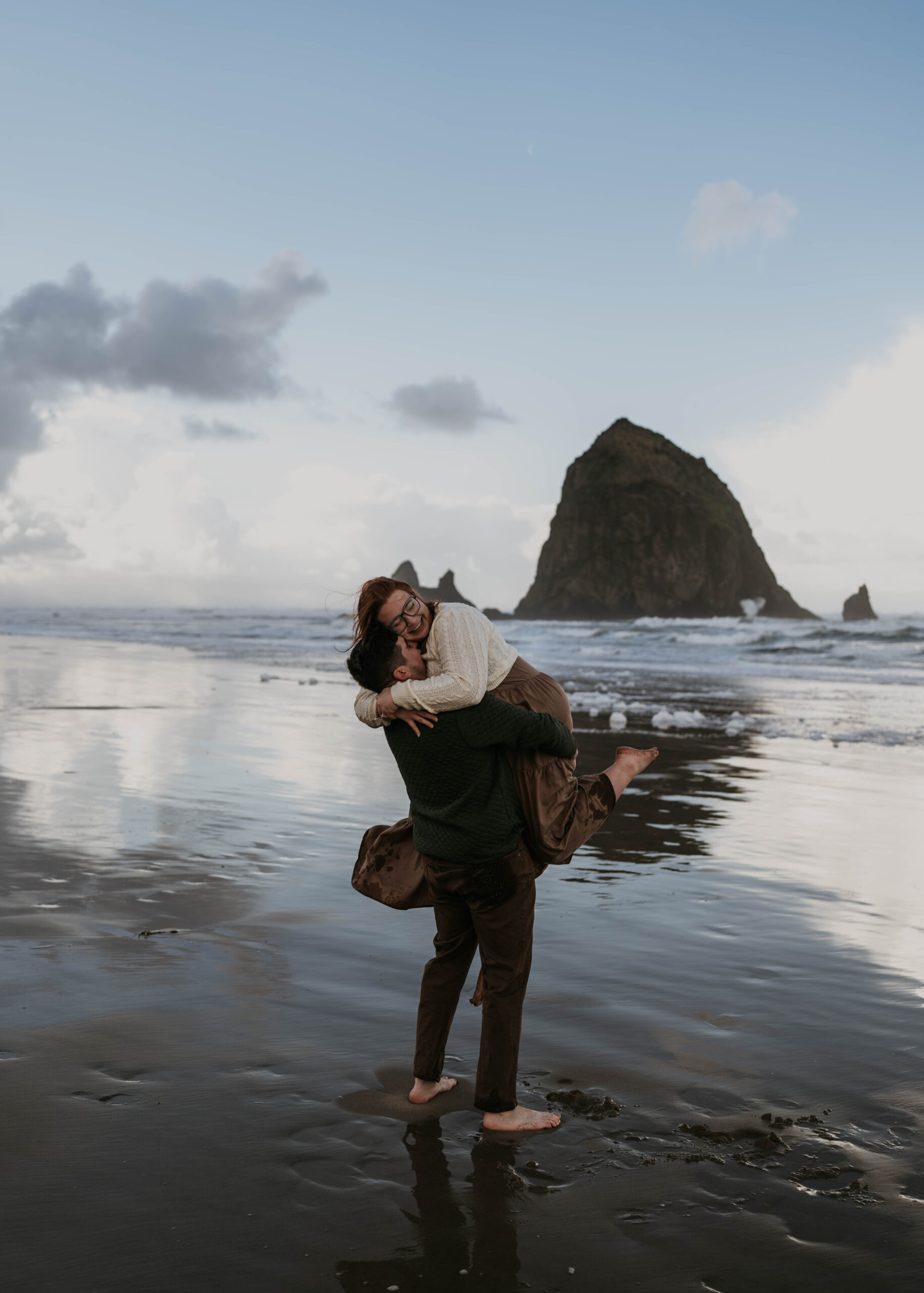 man lifting women up at cannon beach in oregon