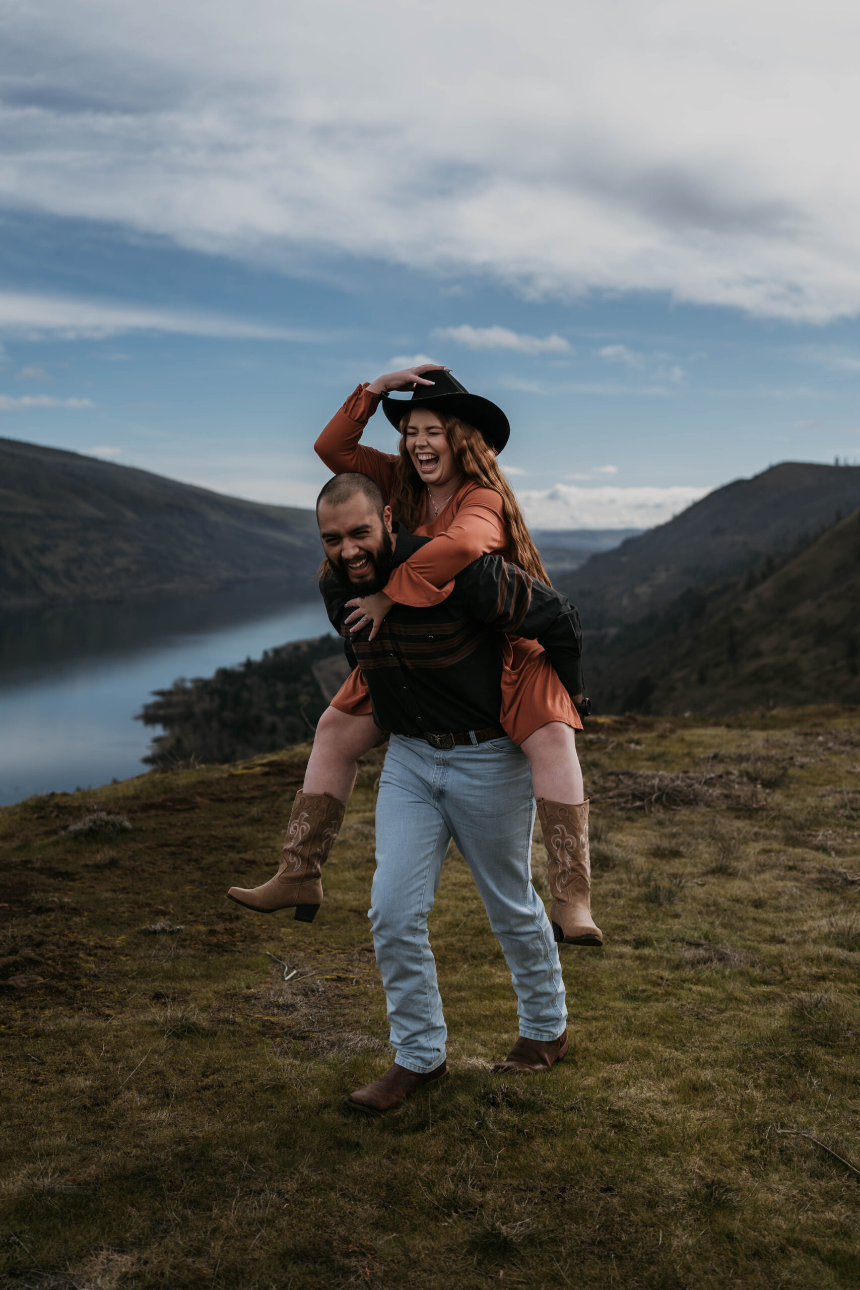 couple doing a piggy back ride in western attire with mountains and river in background