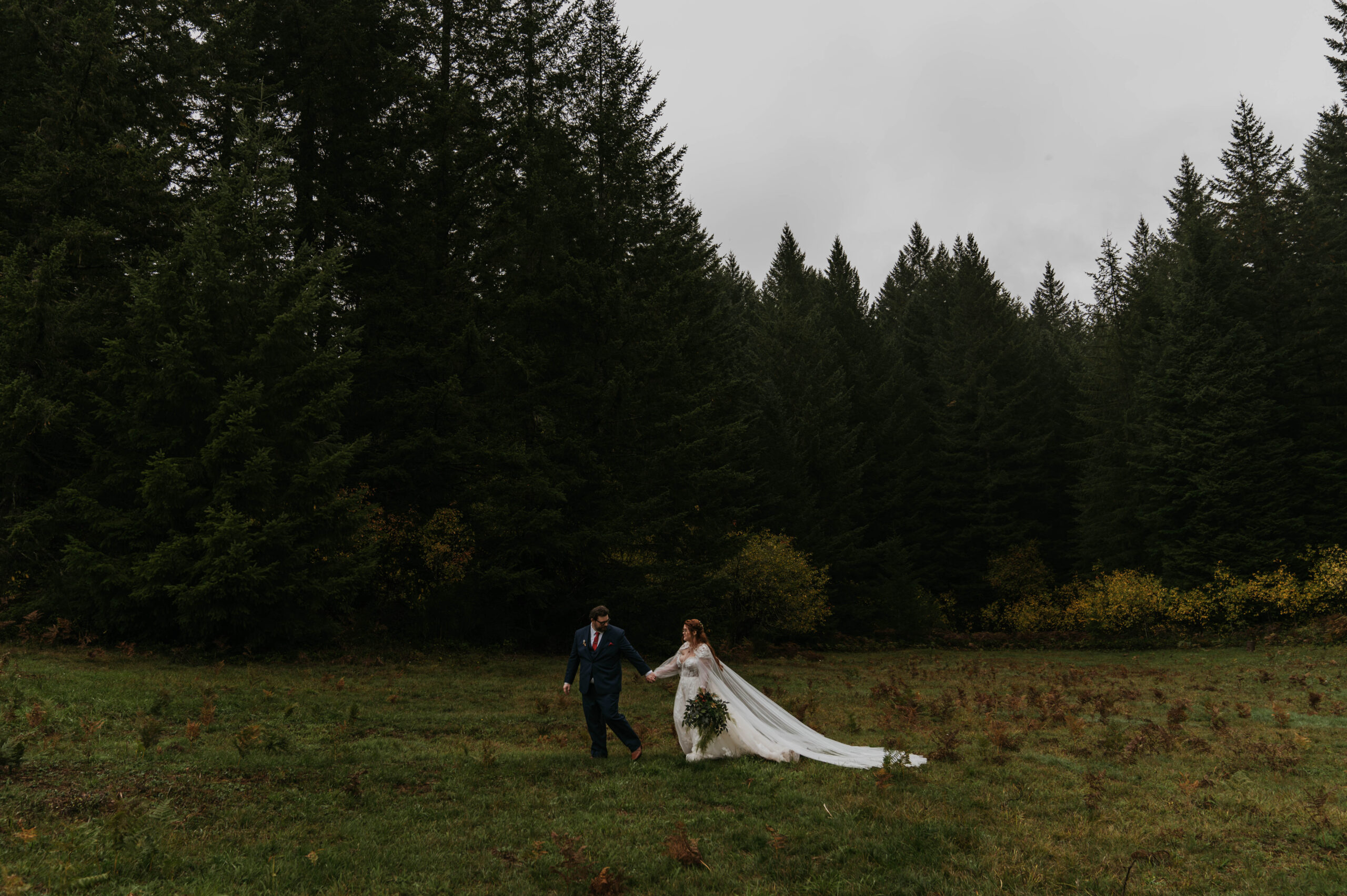 bride and groom holding hands walking on grass with a forest in the background