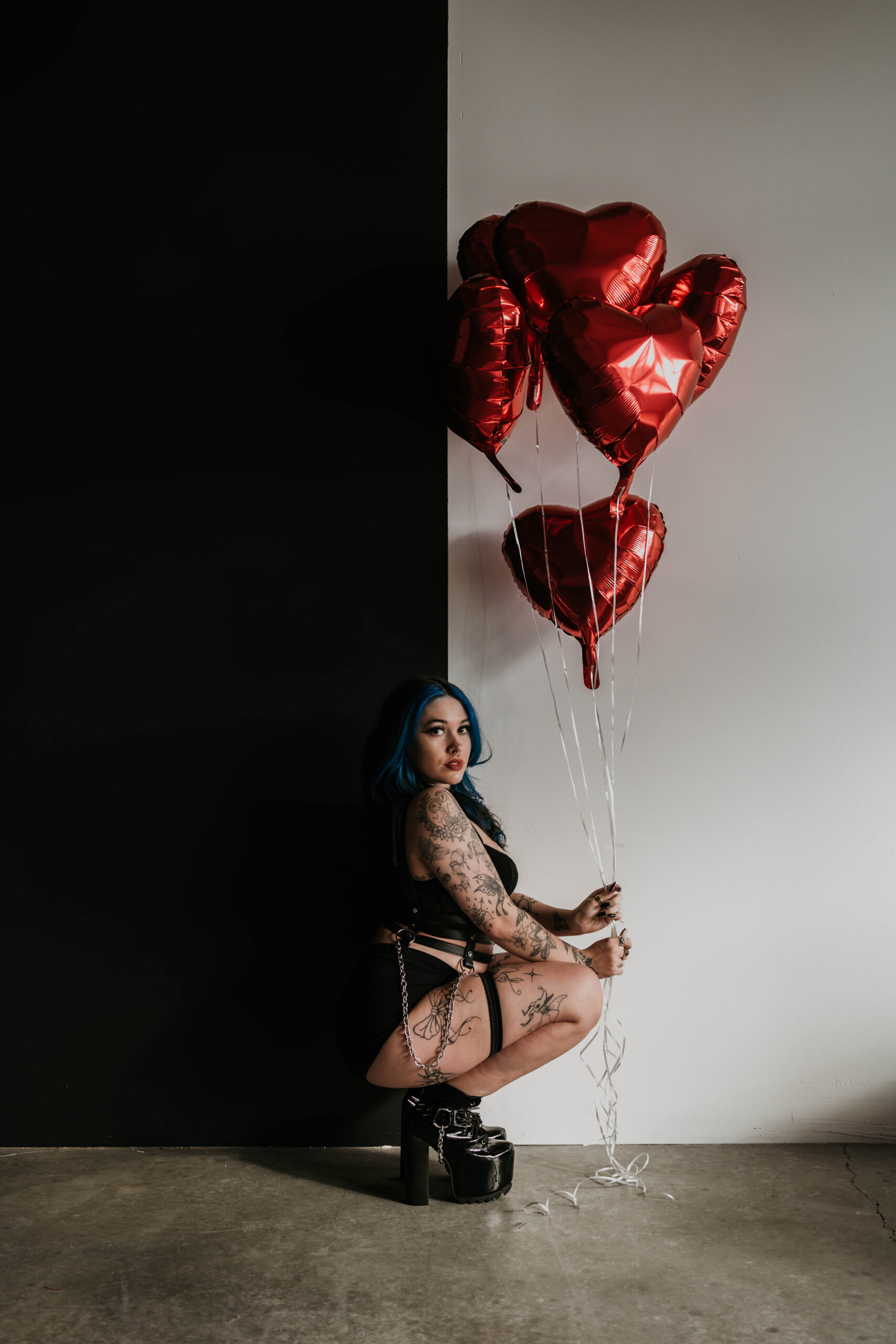 women in front of black and white wall, squatting down in black lingerie holding red heart balloons for valentines shoot