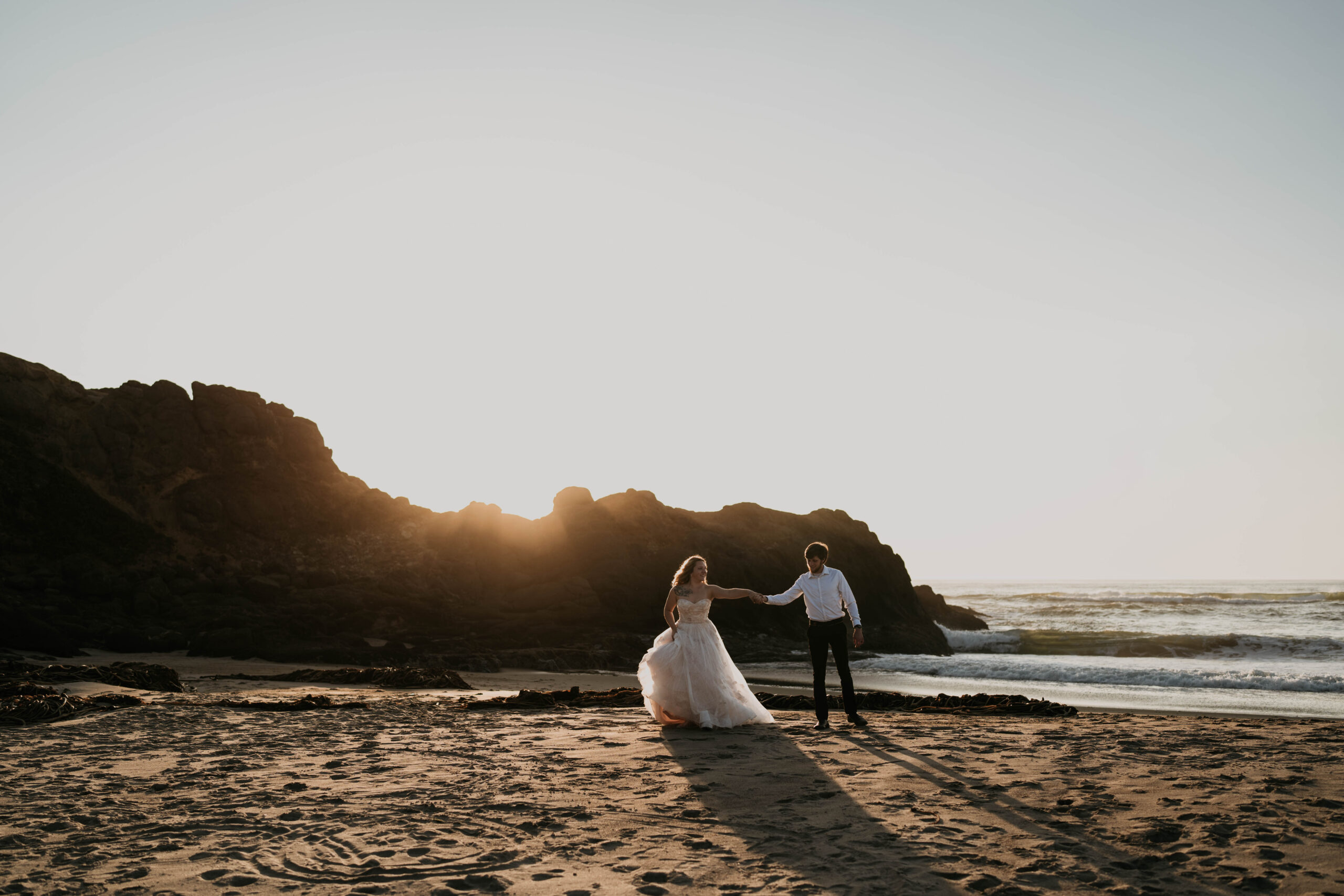 bride and groom holding hands running on beach in sunset