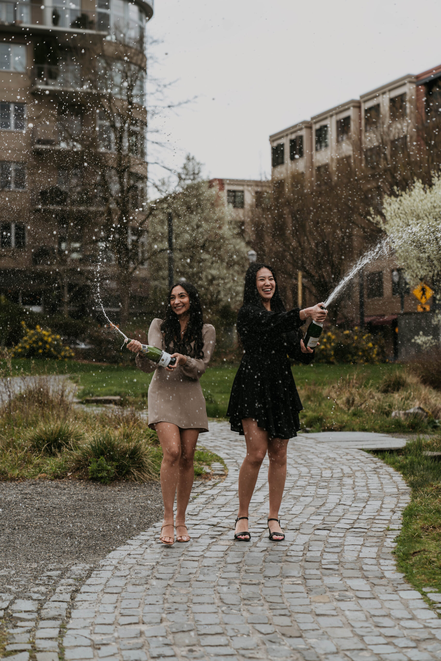 two girls popping and spraying champagne bottle in downtown city park