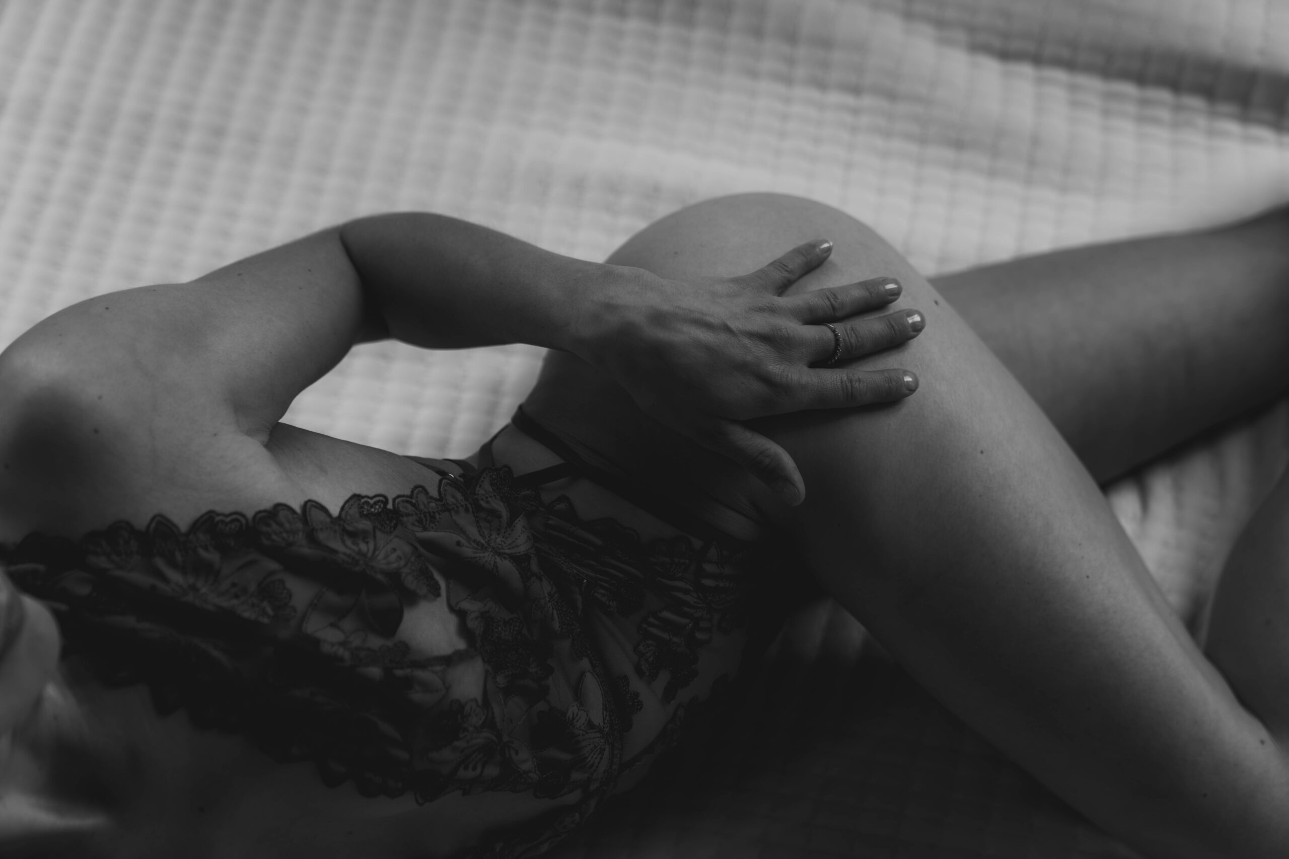 black and white of shoulder to knee of women laying on bed touching thigh in lingerie