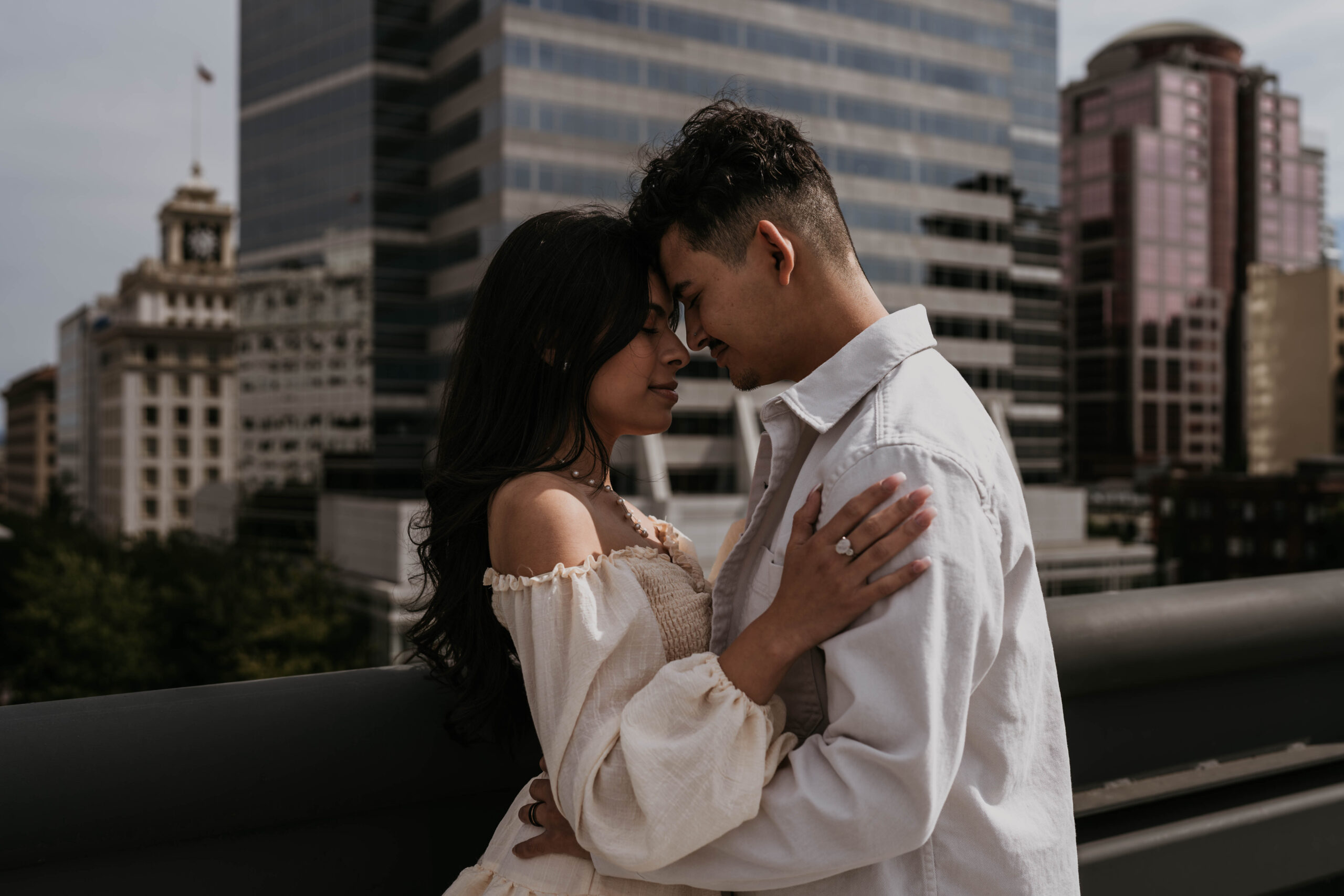 couple holding each other close, forehead to forehead, with city backdrop