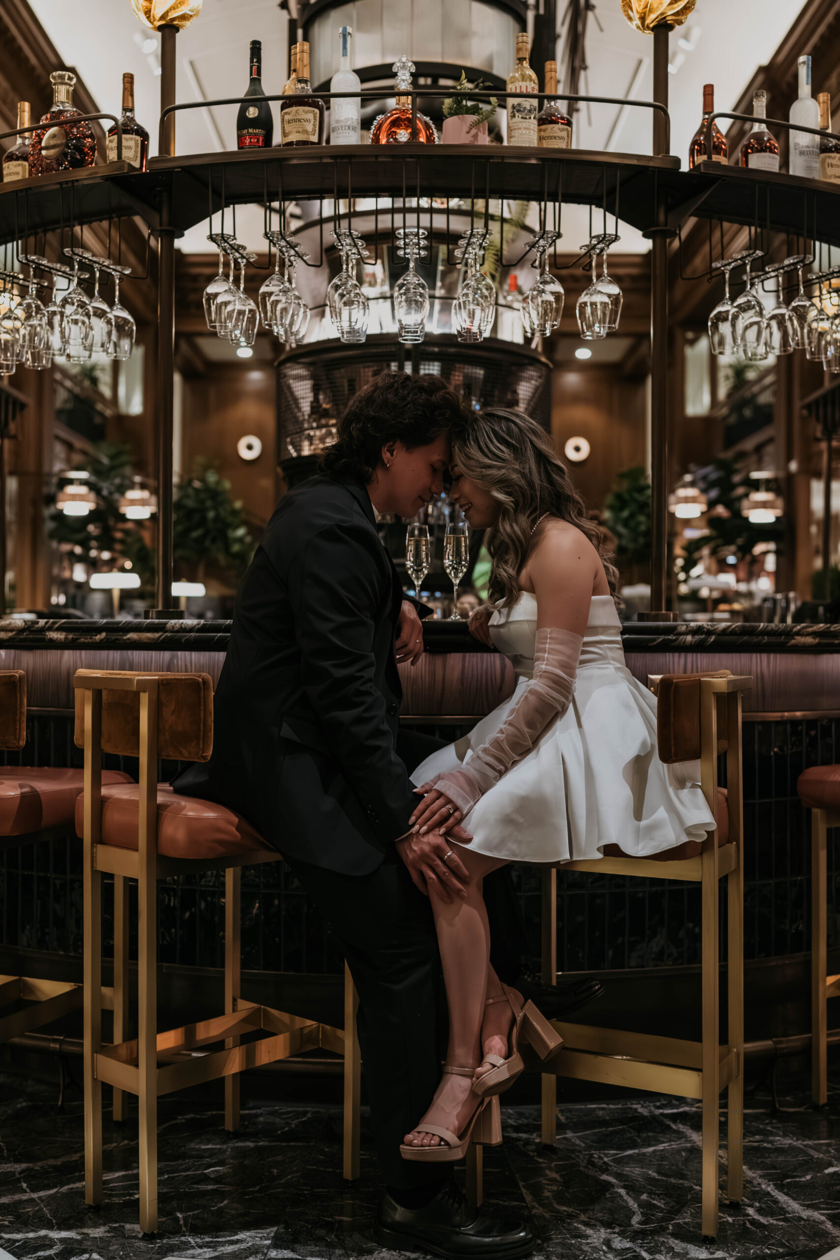 couple in black and white formal attire forehead to forehead sitting at hotel bar