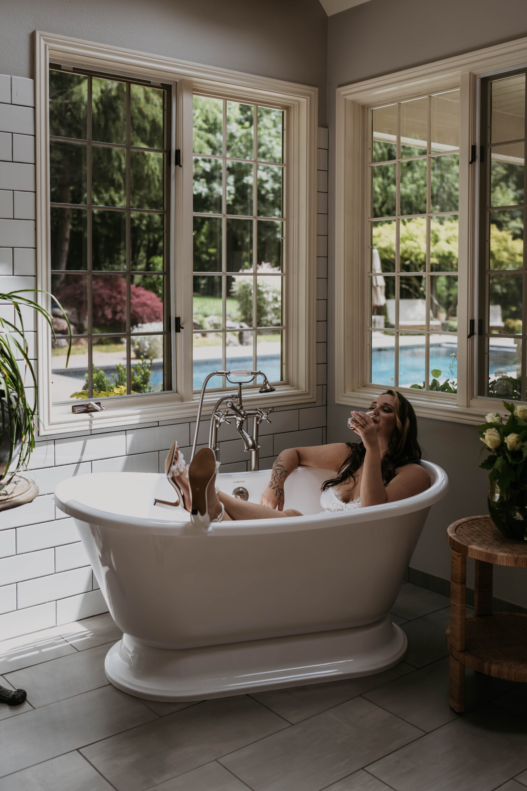 women in big stand alone bath tub in white lingerie playing with hair laughing with big windows behind her