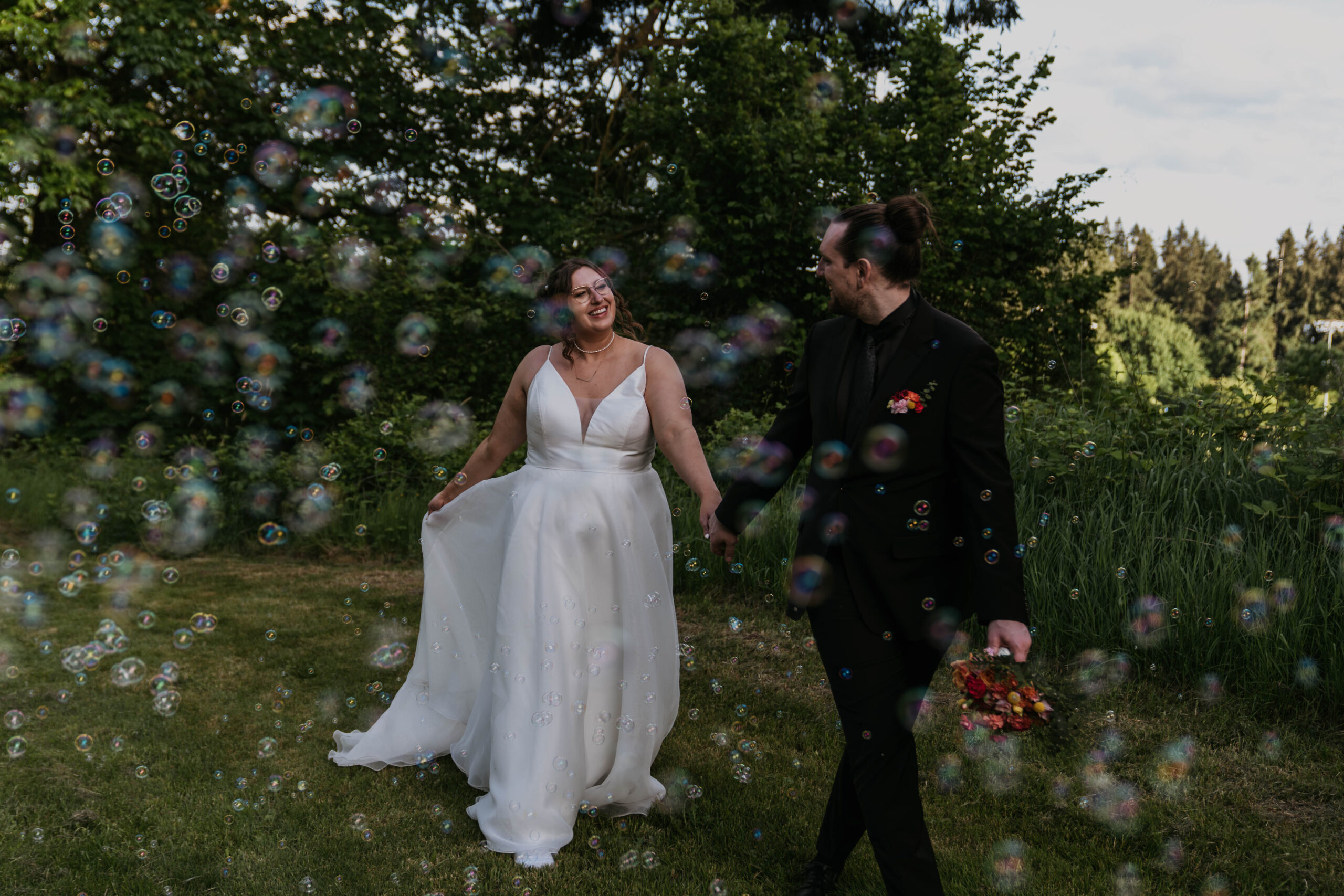 bride and groom holding hands walking through a ton of bubbles in a forest