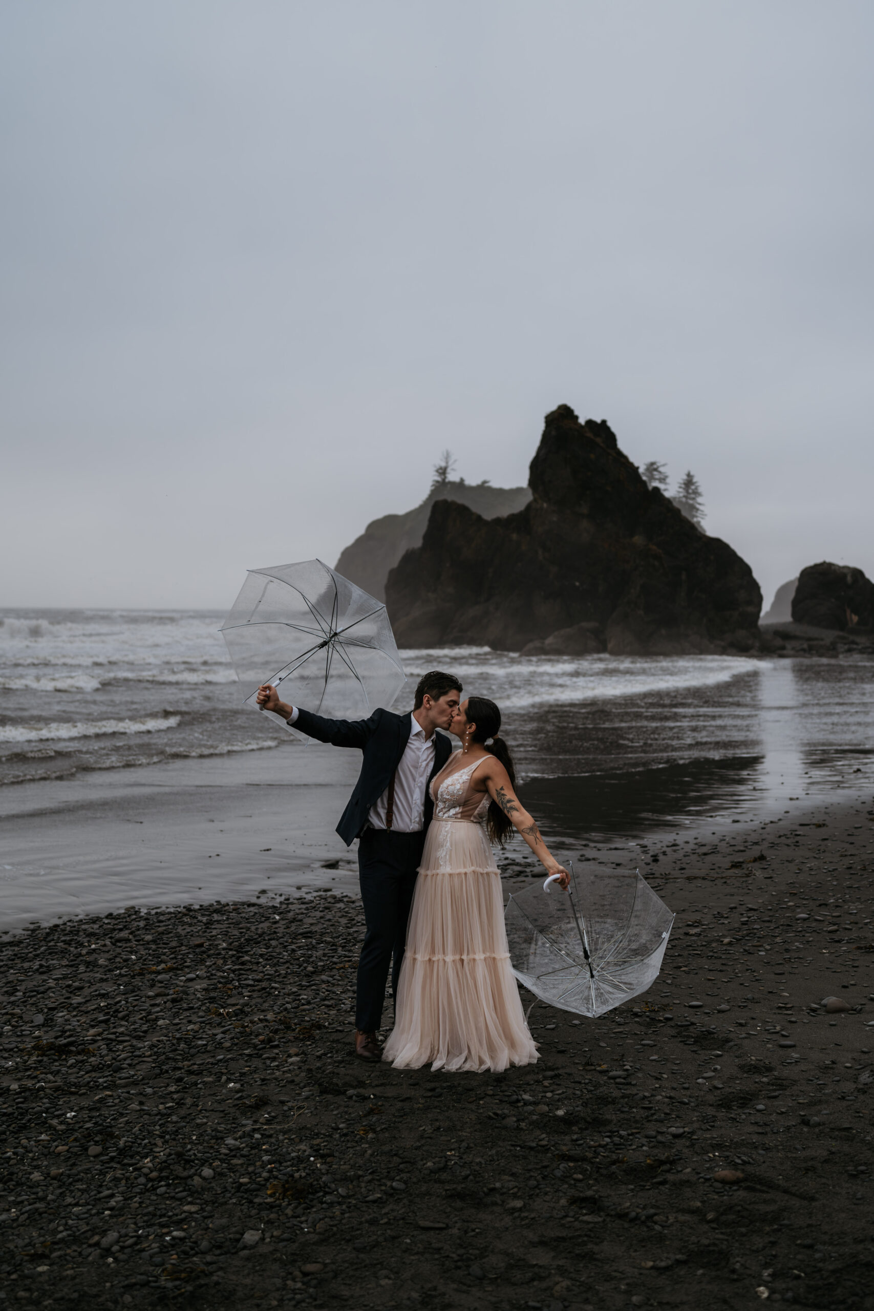 bride and groom on beach kissing holding umbrellas in moody weather