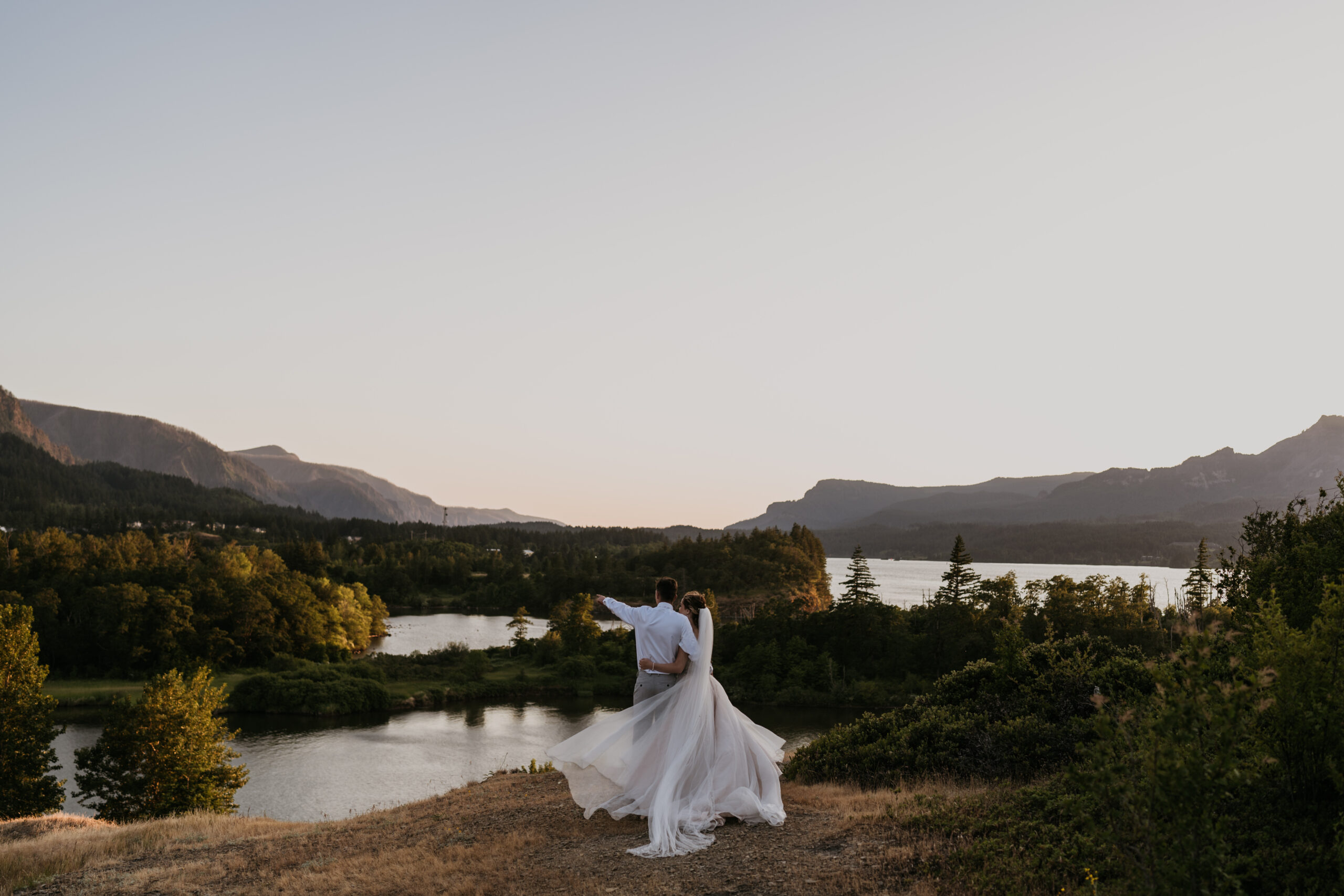 bride and groom standing on cliff looking at mountain river view