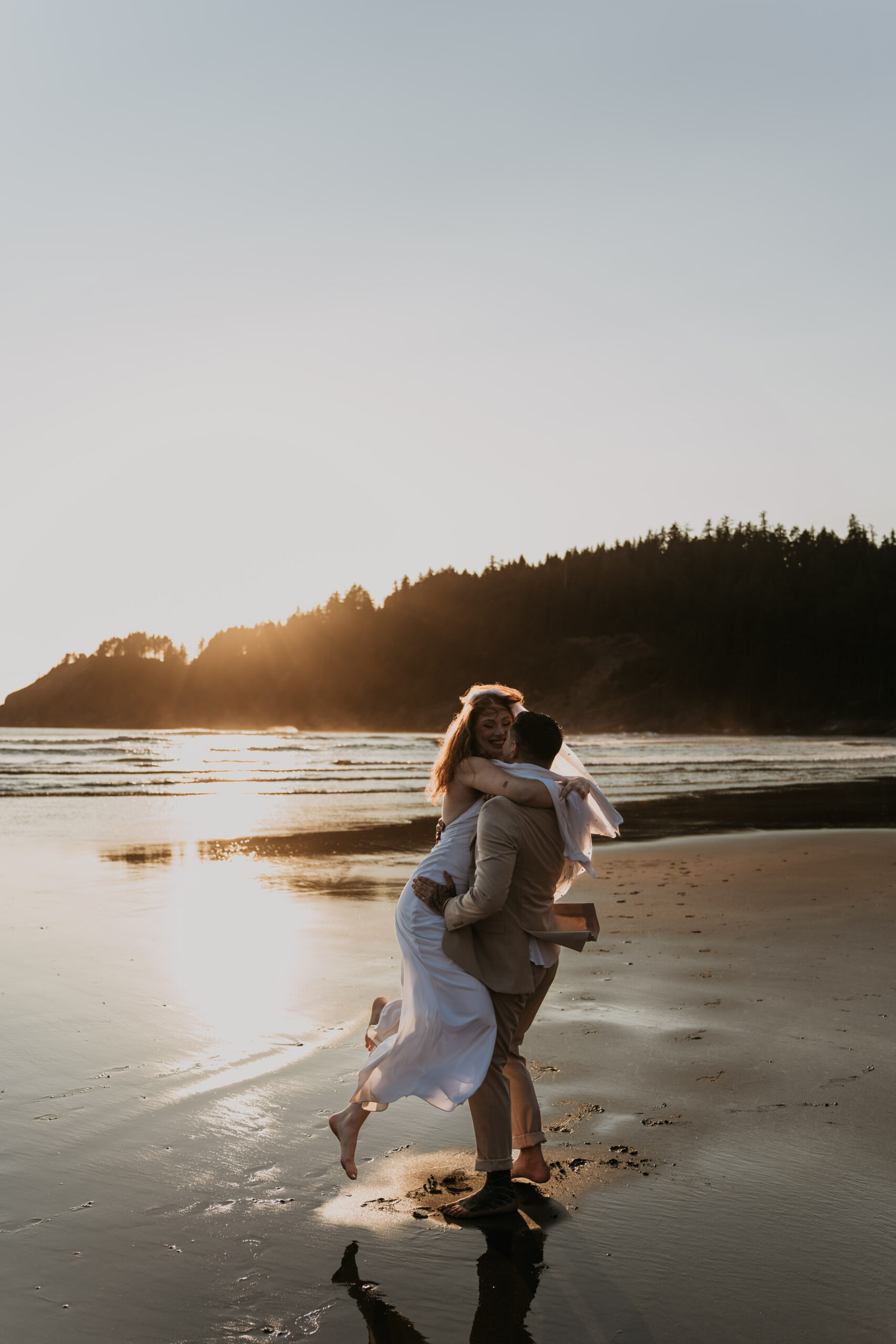 groom lifting up bride on beach twirling around laughing with golden hour sunset