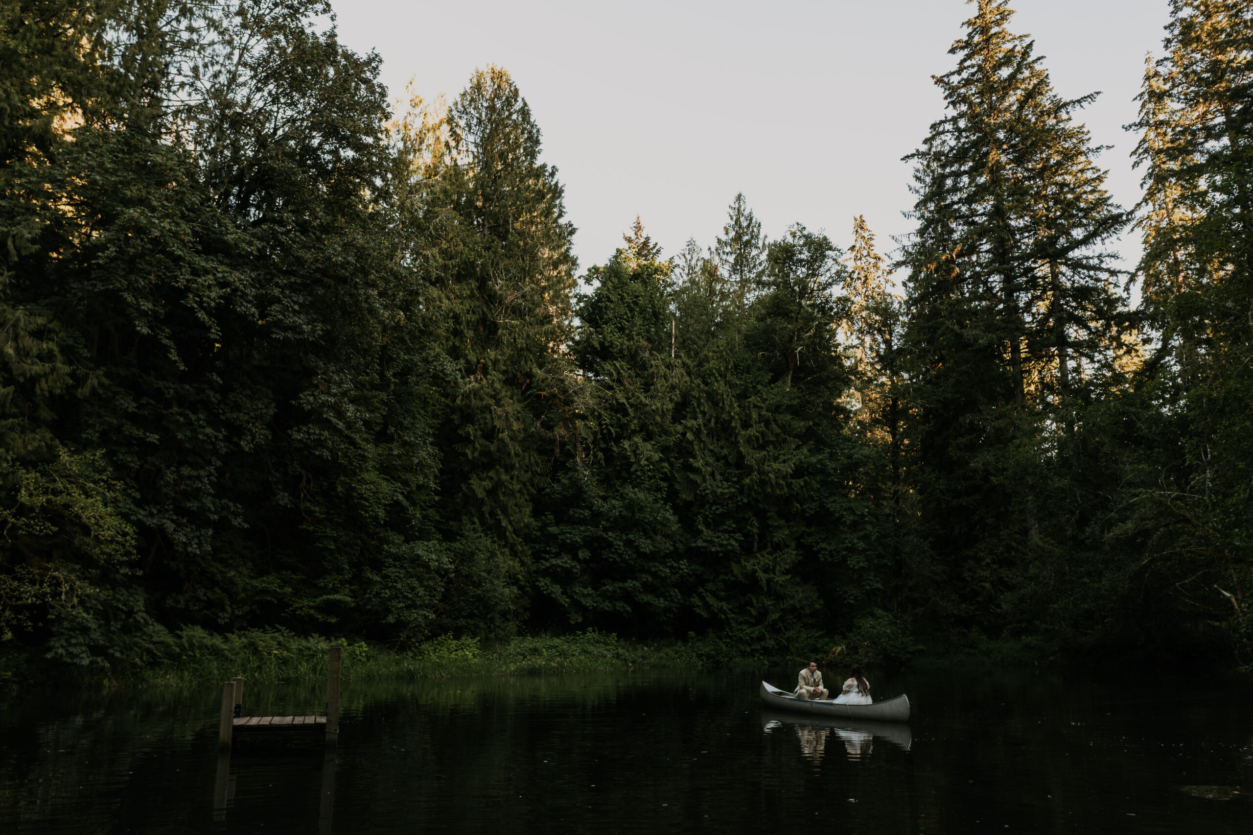 bride and groom in canoe in lake surrounded by heavy forest during sunset