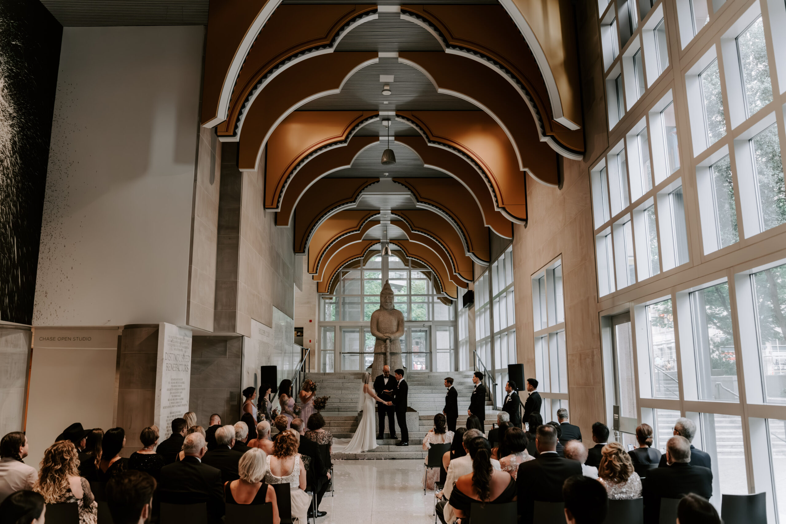 bride and groom at alter of indoor venue with architecture and full of windows during ceremony