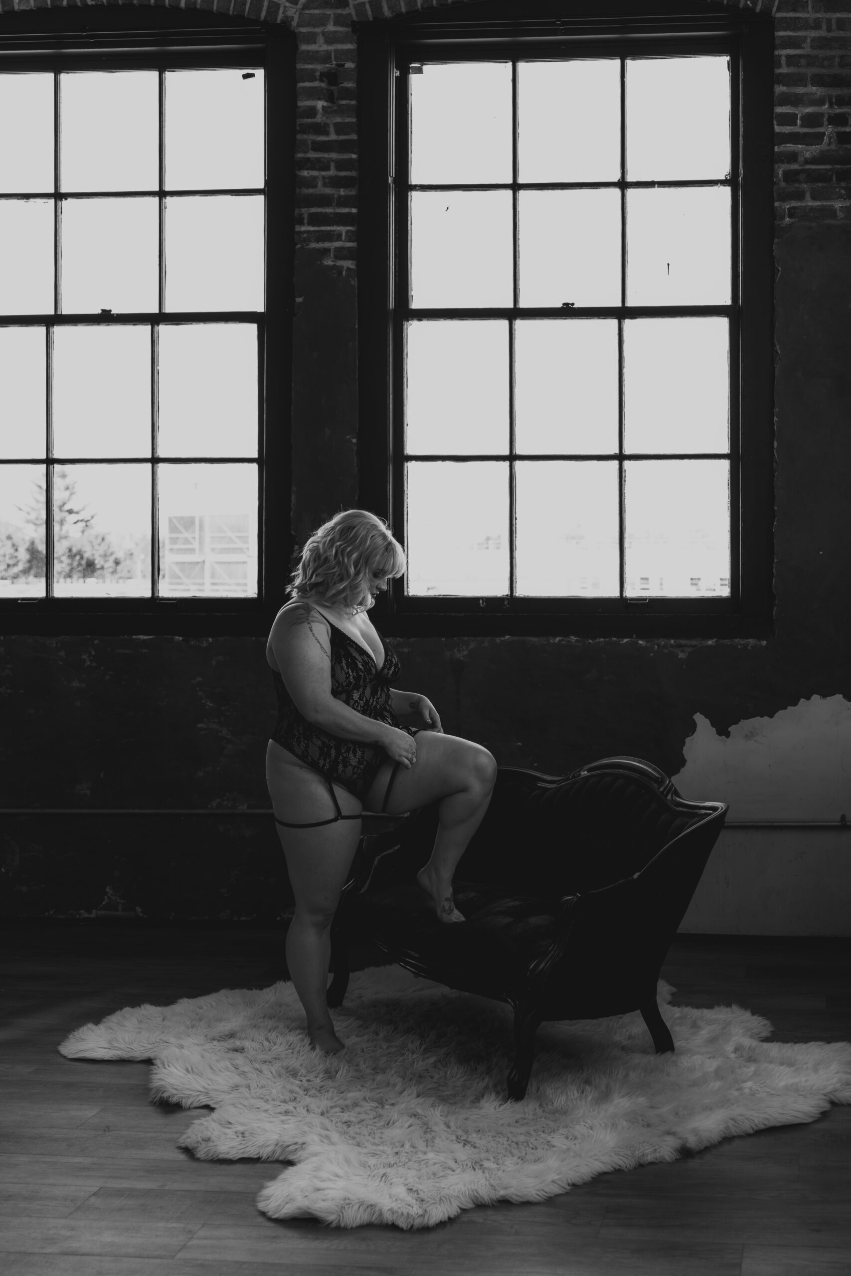 black and white of women in lingerie with leg on couch in front of windows for boudoir shoot