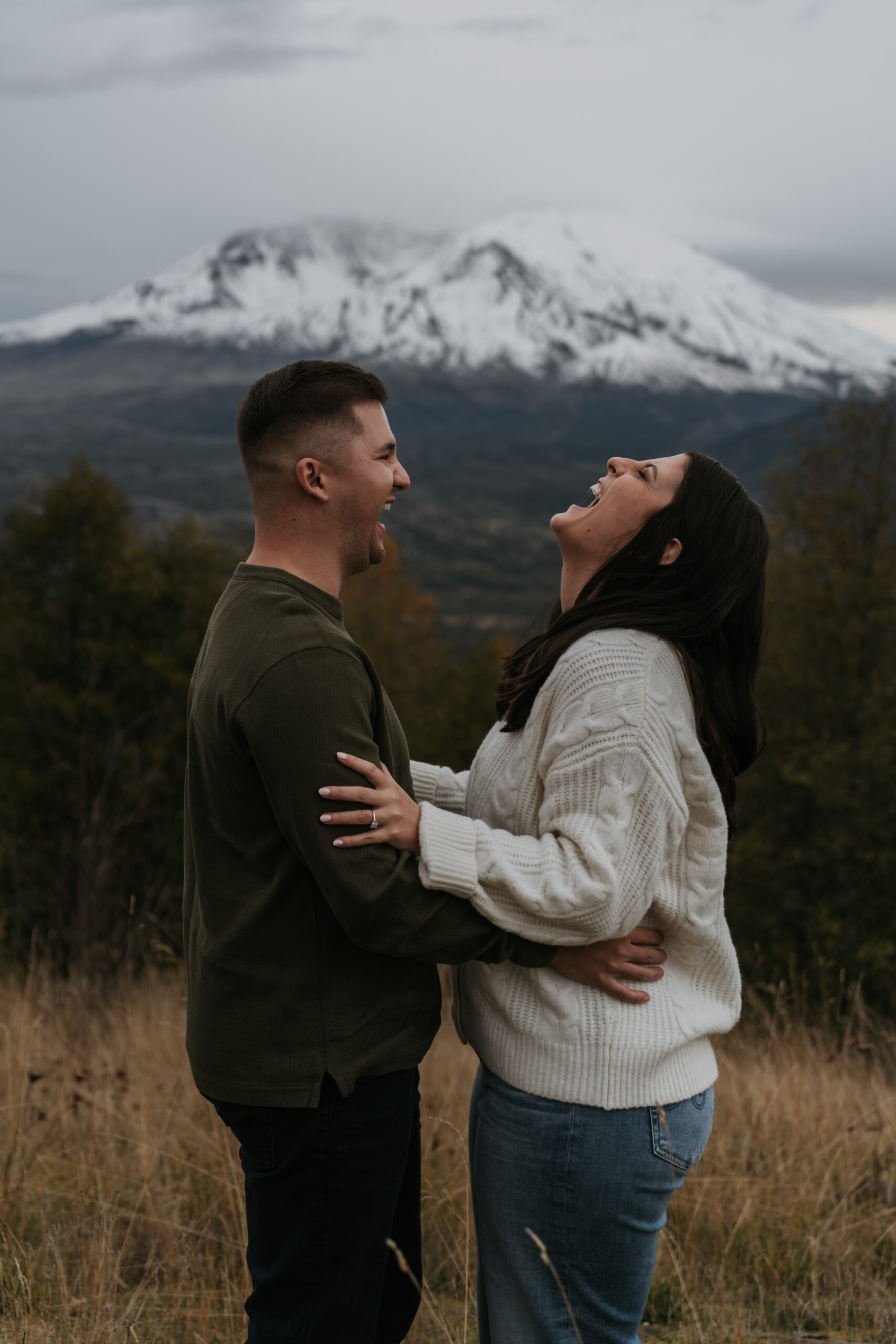 couple holding each other laughing really hard with mountain in backdrop