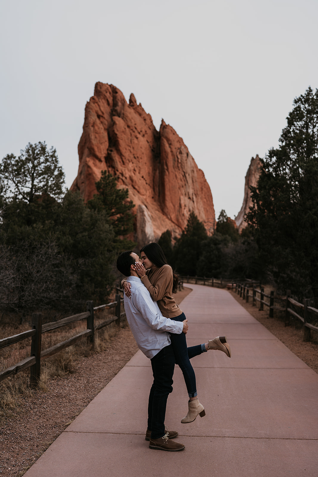man lifting up women kissing on path with rocky and forest near them