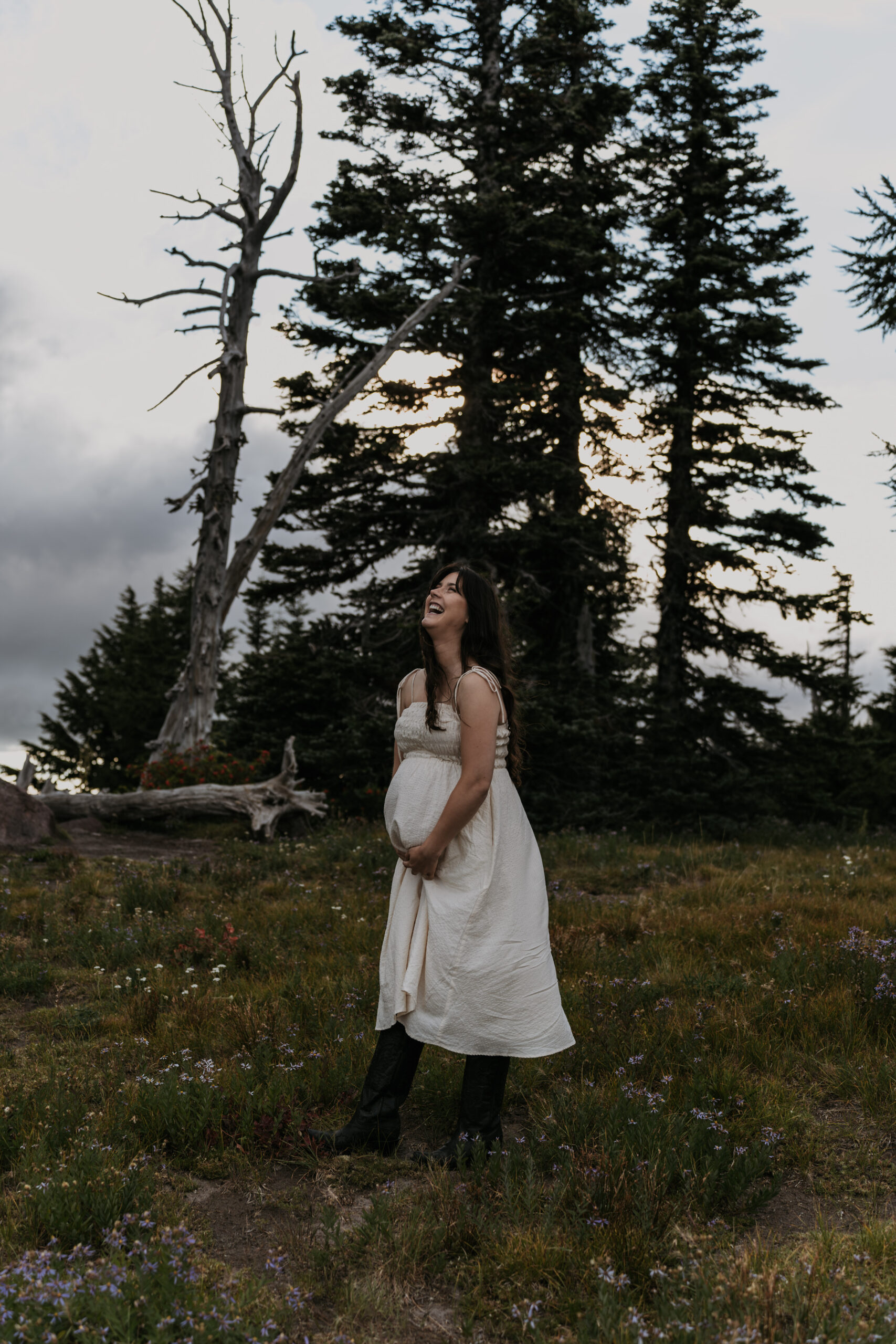 pregnant women holding belly in meadow and forest laughing