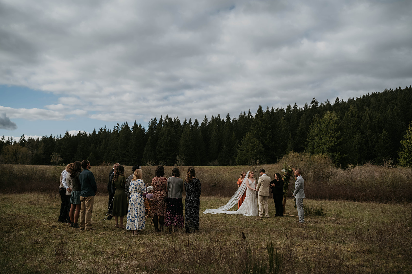 bride and groom getting married with a few family and friends surrounding them in a forest on cloudy day
