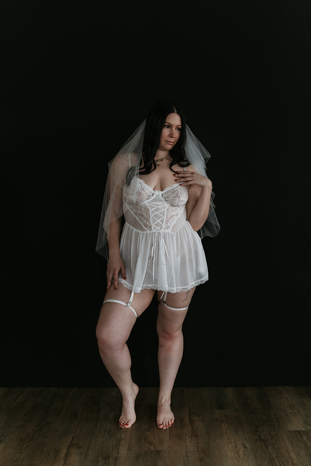 women in white bridal lingerie with veil standing with black backdrop