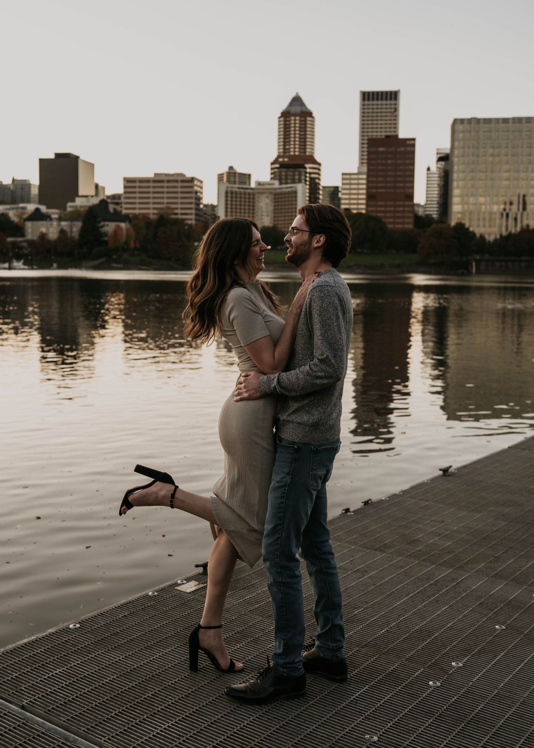 couple holding each other on dock with water and city backdrop