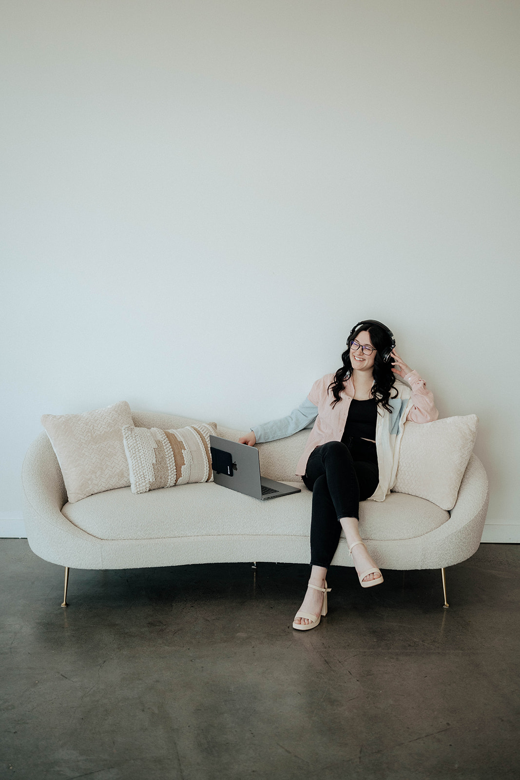 women sitting on couch with laptop, headphones, and mic recording podcast