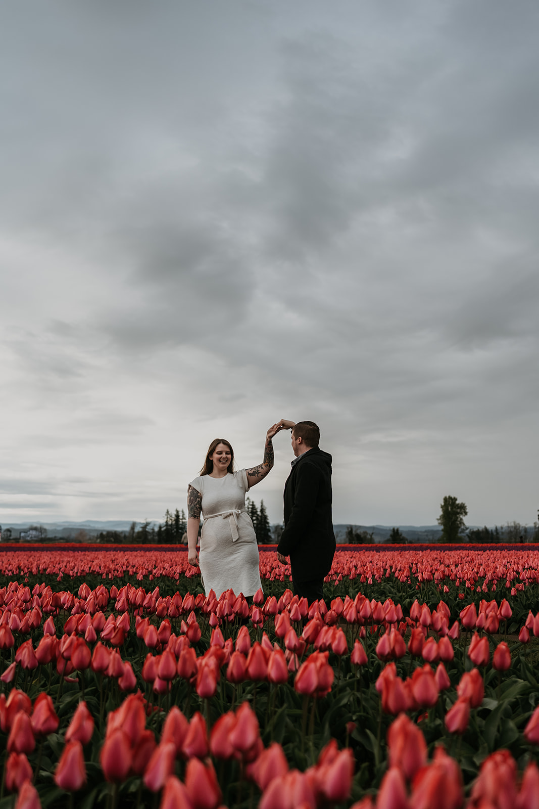 man twirling women around in a bed of tulips on a cloudy day