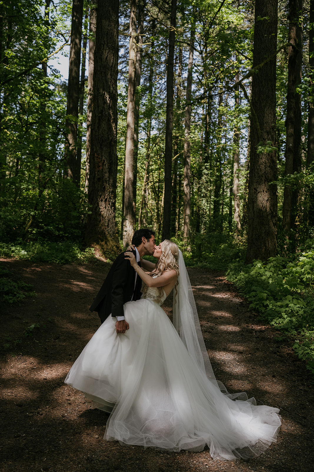 groom kissing bride dipping her back holding each other while in a forest