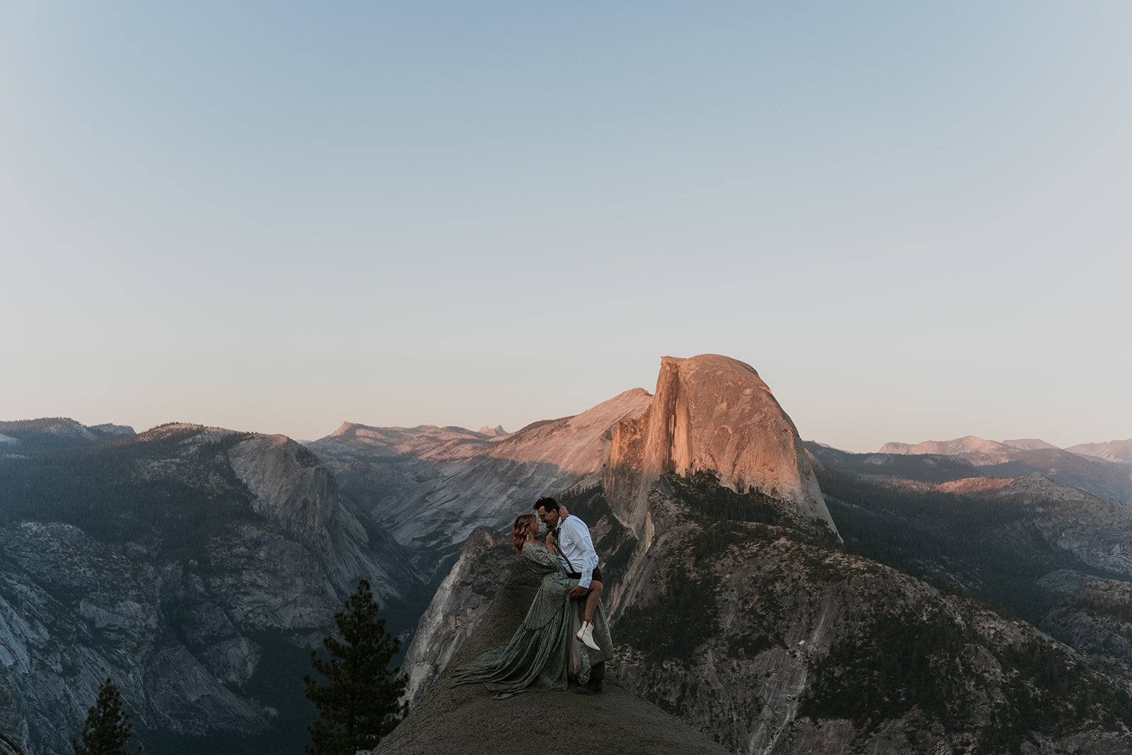 couple kissing on large rock during sunset with big rocks in background at Yosemite National Park