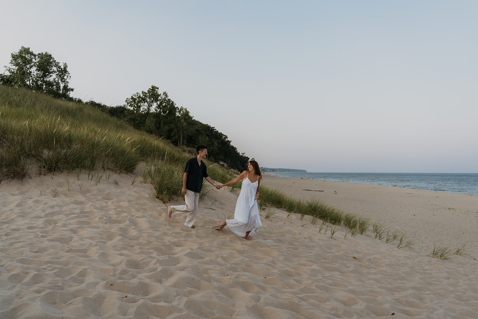 women and man running down sand dune holding hands with tall grass nearby