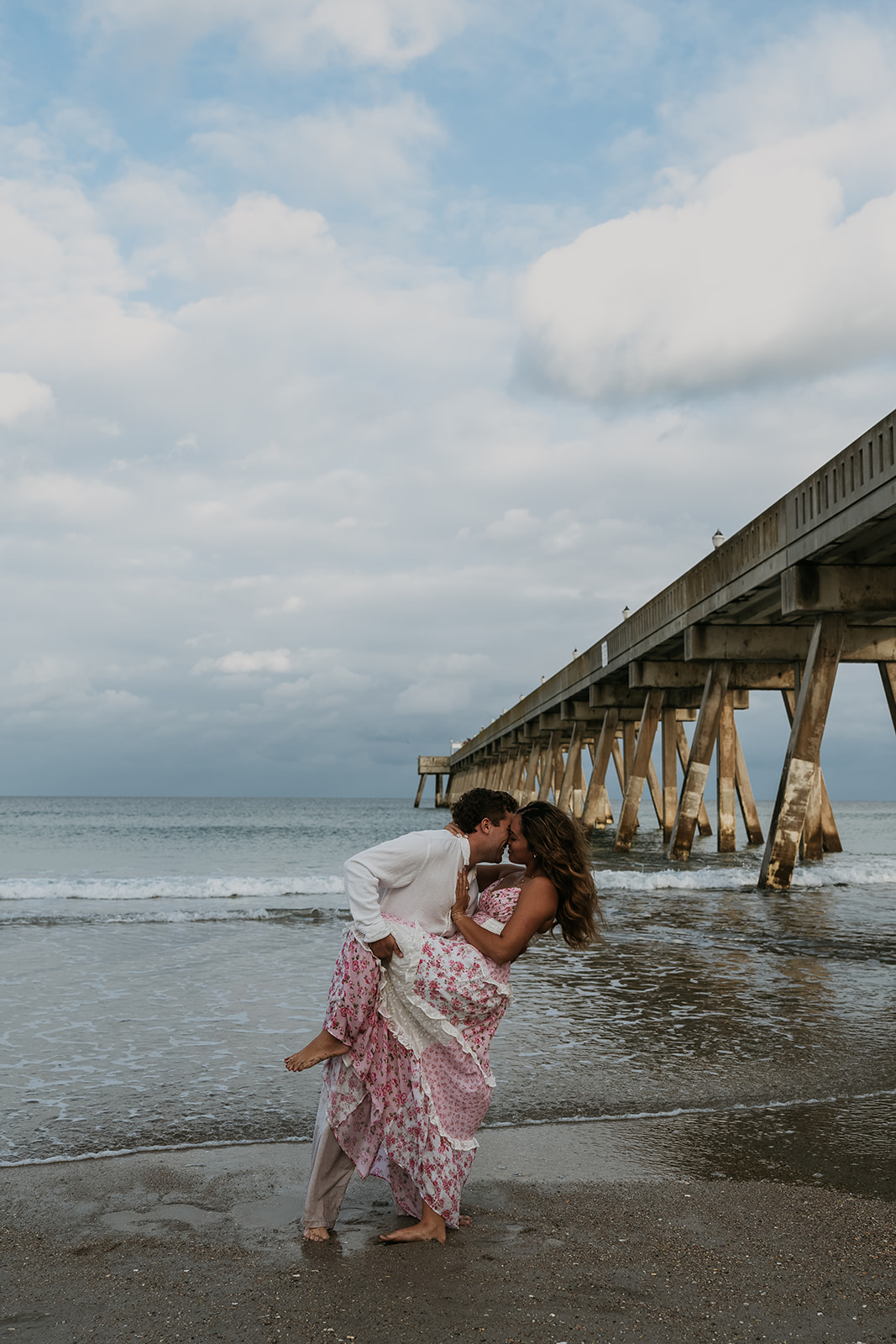 man dipping women kissing in front of pier at beach in North Carolina
