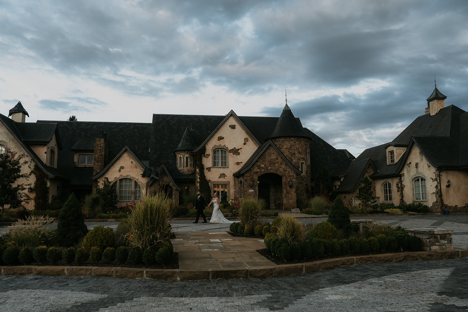 bride and groom walking together holding hands in front of a stunning chateau European wedding venue on a cloudy day