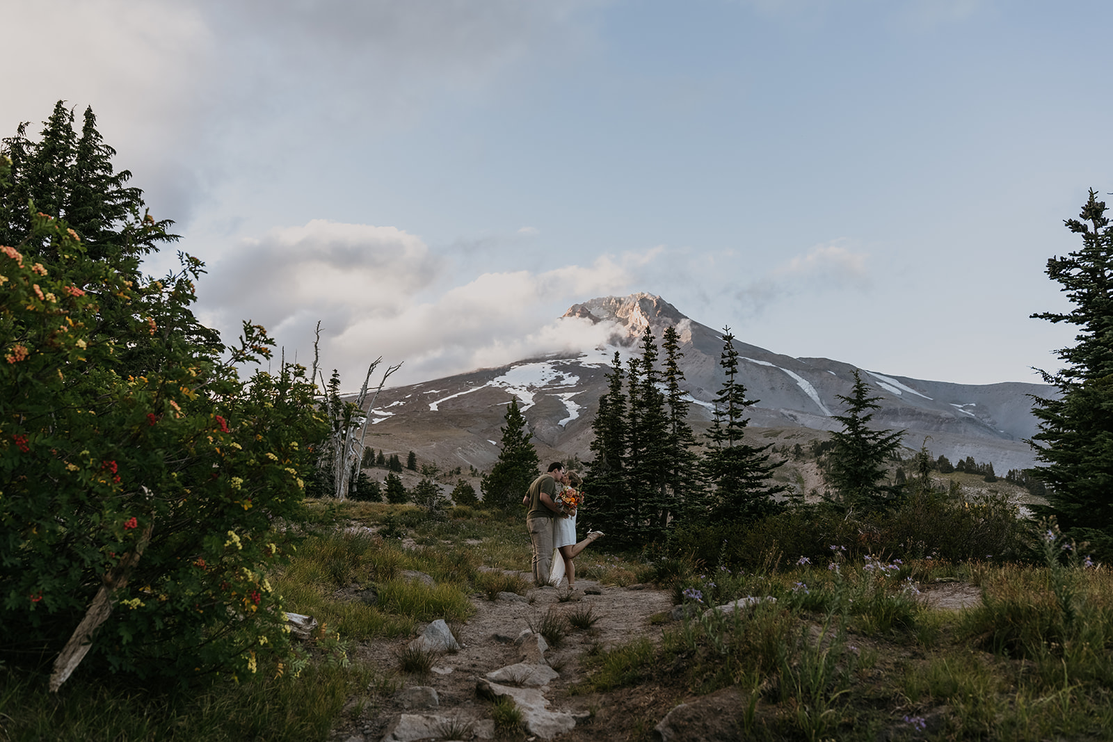 bride and groom standing kissing surrounded by forest with giant mountain in background