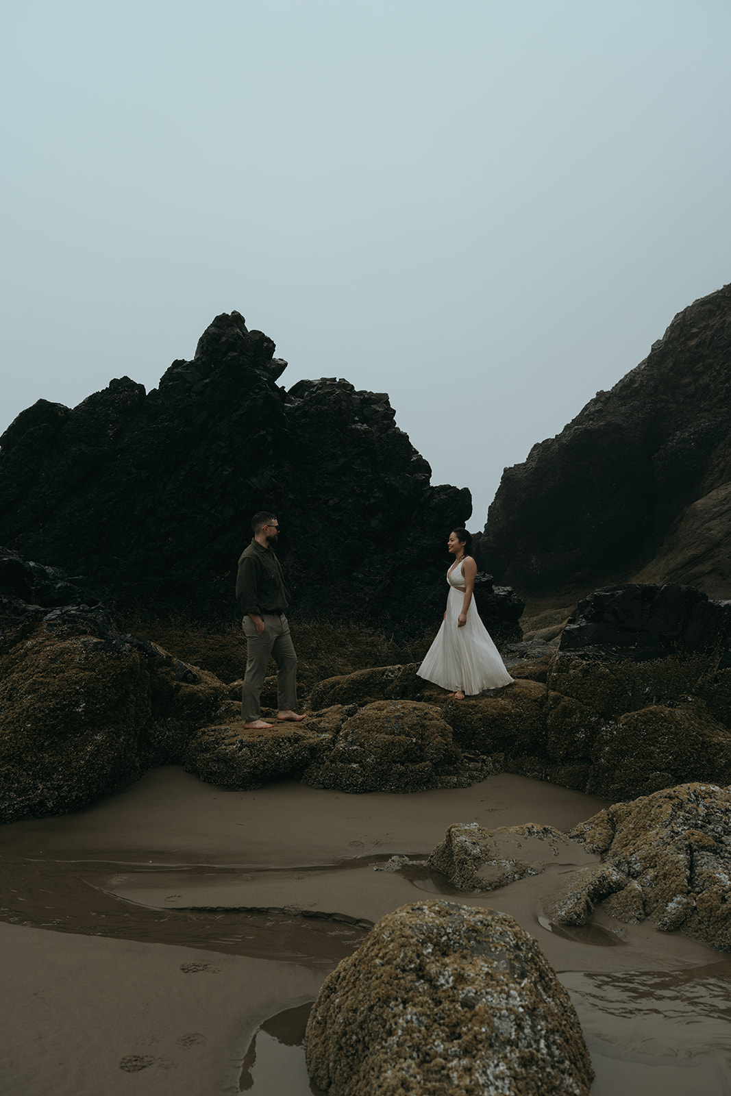 couple standing on rocks at beach twirling around in a foggy weather day