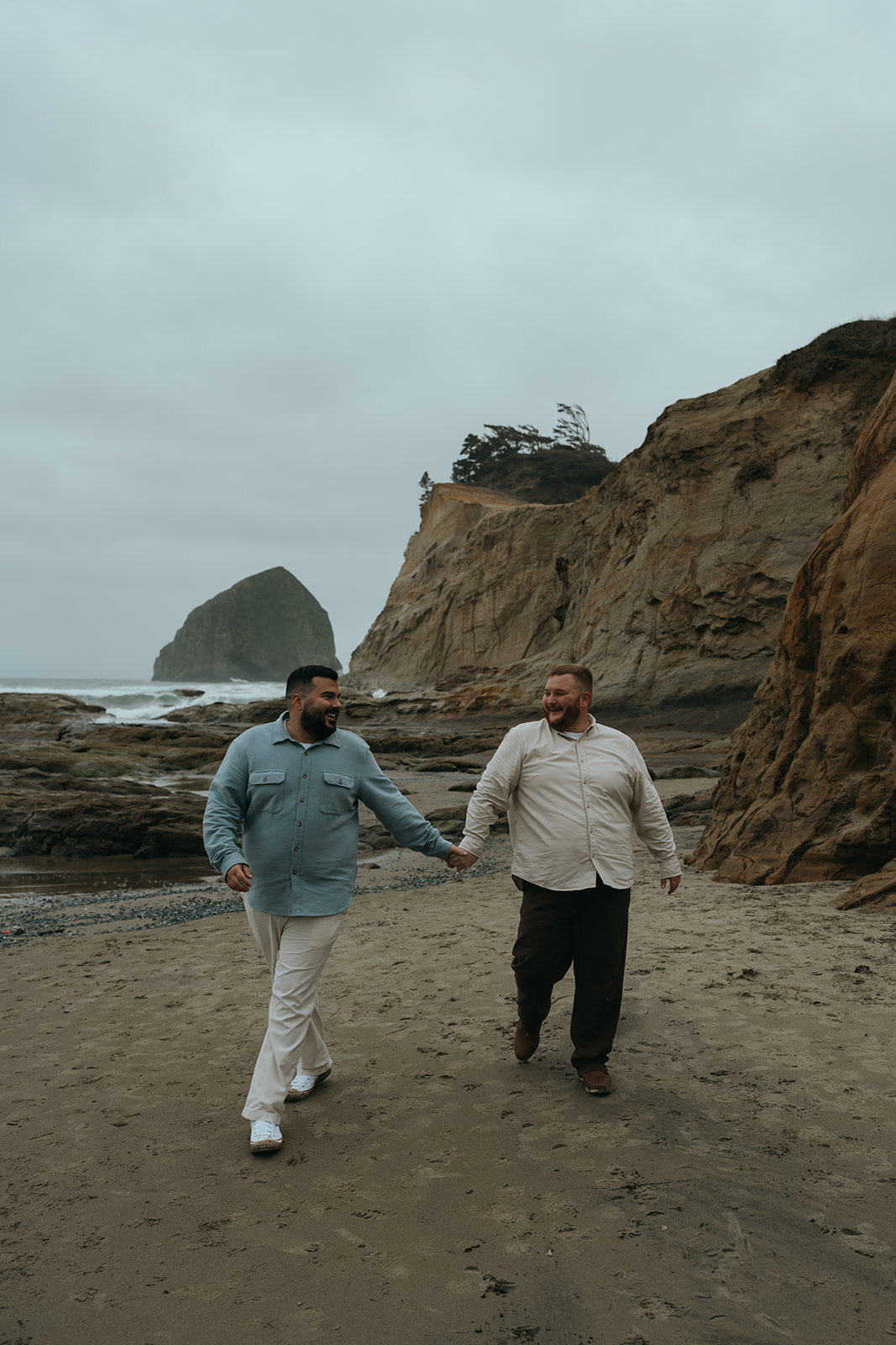 two men holding hands walking on beach with many rocky backdrops surrounding with ocean