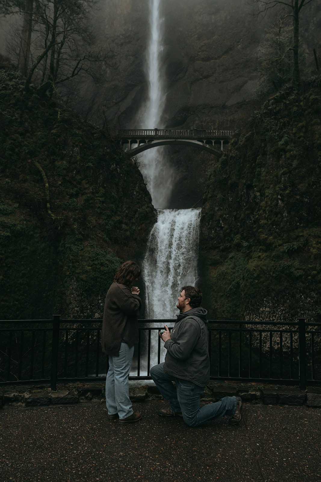 man kneeling on one knee proposing to women who's smiling with a big waterfall behind them