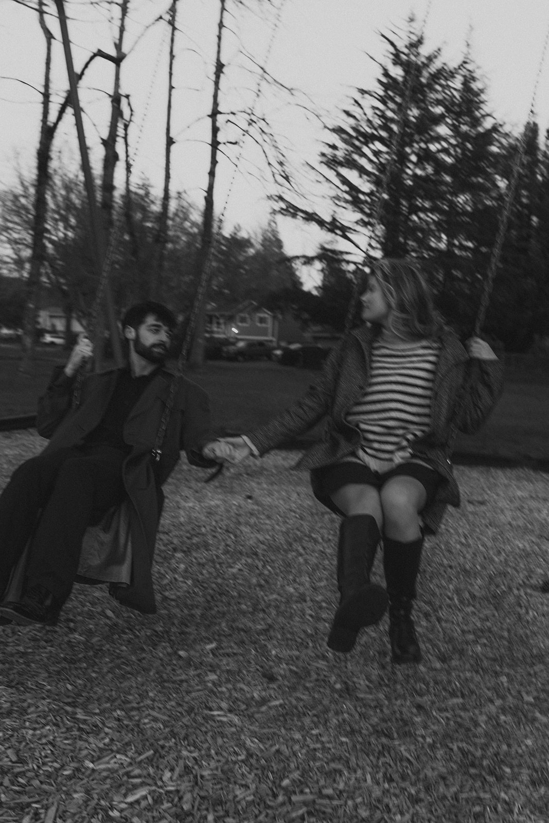 black and white of man and women holding hands on swing set at playground