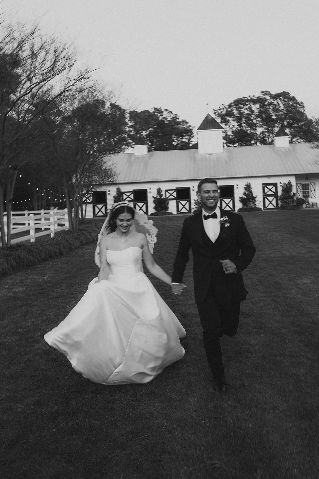 black and white of bride and groom running holding hands in front of estate in wedding attire blurry