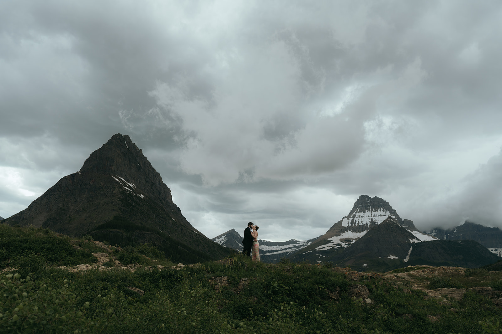 couple kissing in between multiple mountain peeks on a super moody cloudy day