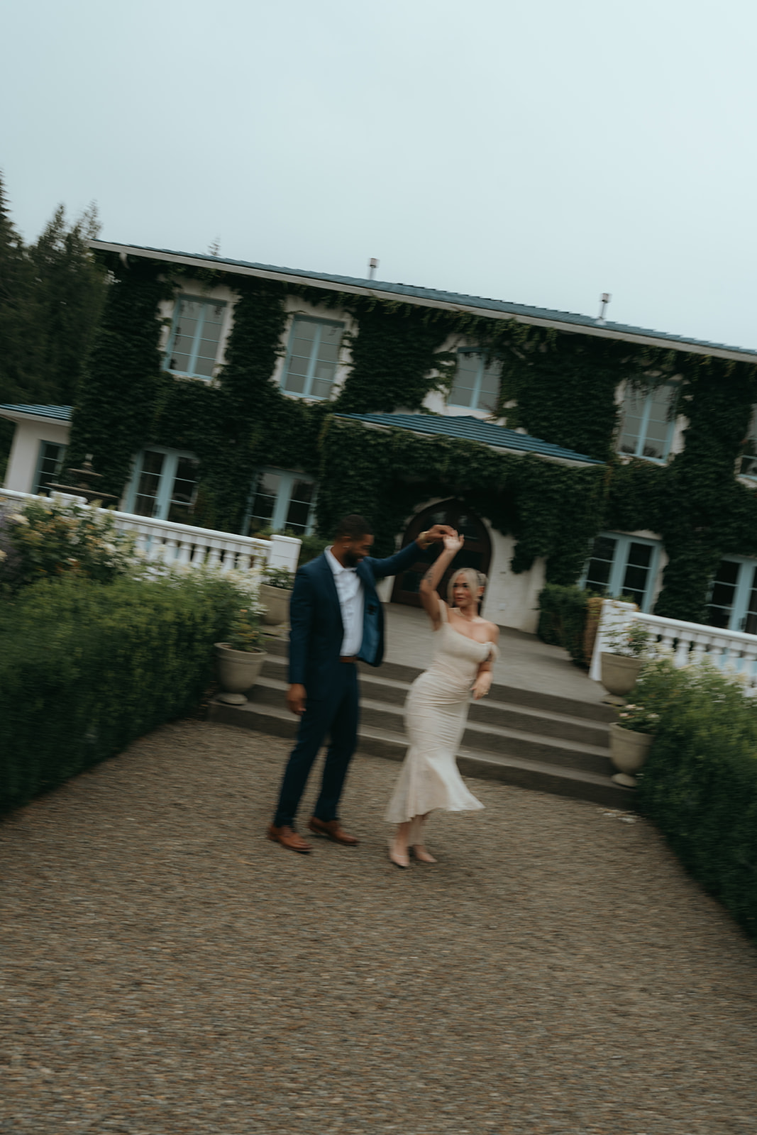 semi blurry motion photo of man spinning women around in front of a vine covered venue