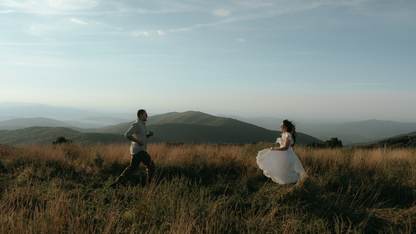 couple running towards each other during sunset on top of a mountain with blue skies