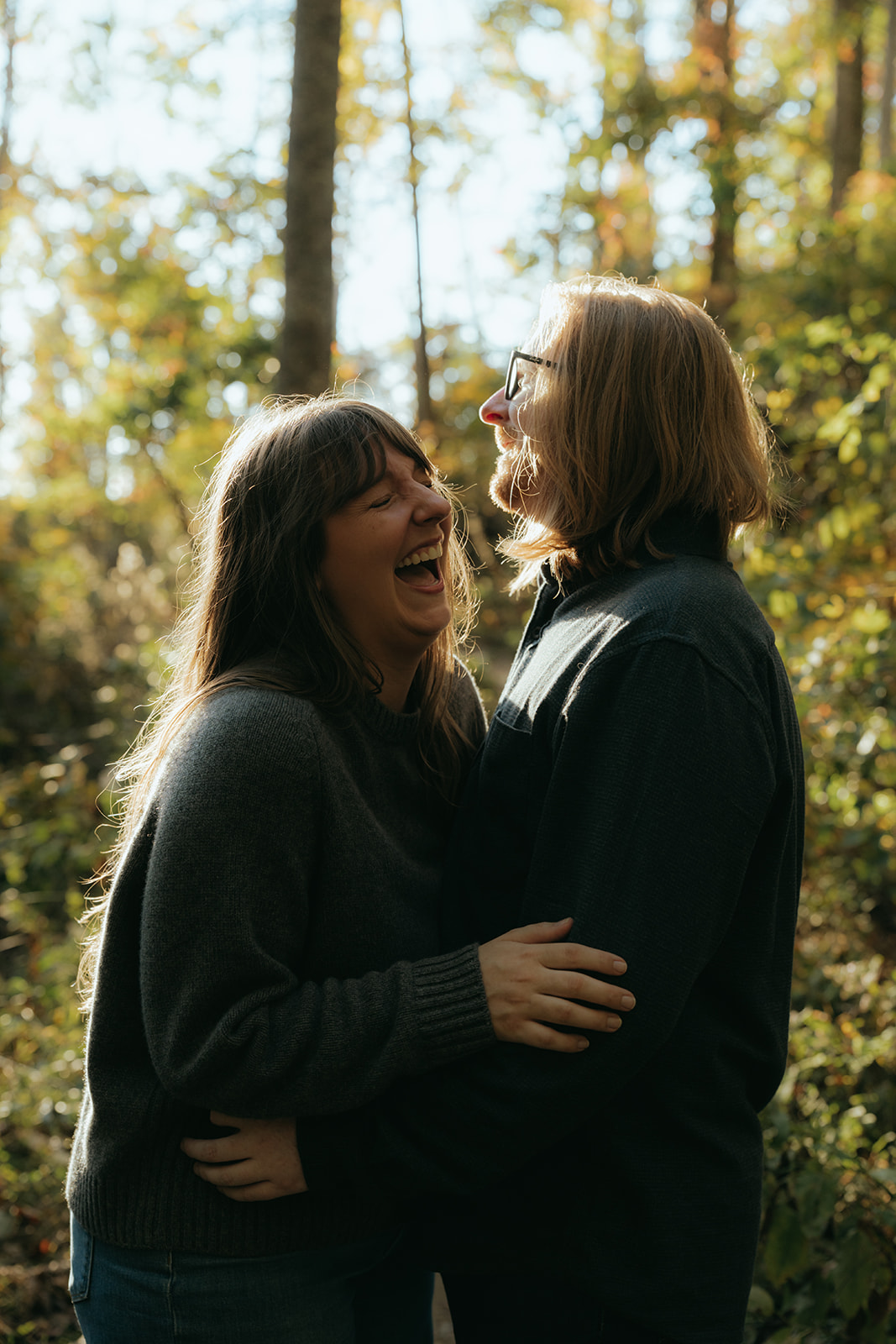 man and women holding each other laughing in the forest with sun shining on them
